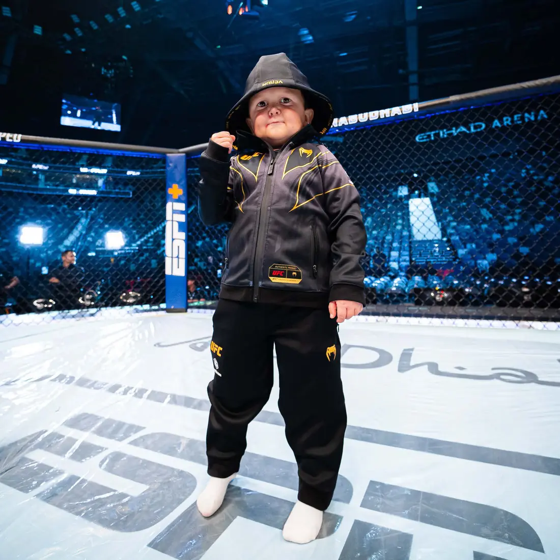 Hasbulla Magomedov standing in the UFC Octagon in a hoodie, fist raised